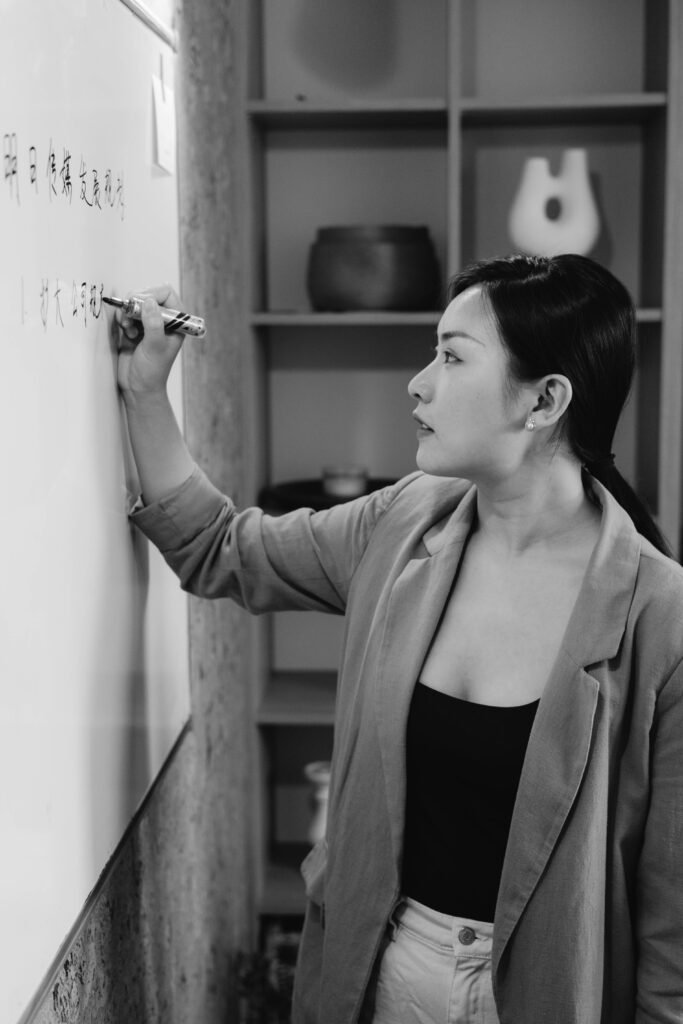 pexels-photo-8519078-8519078 Asian businesswoman writing on a whiteboard in grayscale, captured in profile view.